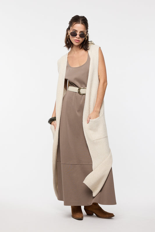 Woman wearing a long beige vest over a brown dress on a white background