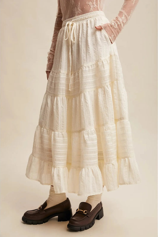 Person wearing a long, light-colored skirt with a neutral background