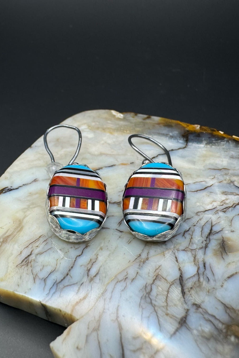 Colorful earrings on a piece of polished stone with a dark background