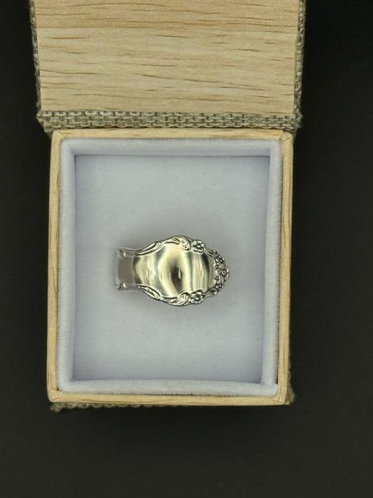 Silver ring with intricate design in a box on a dark background