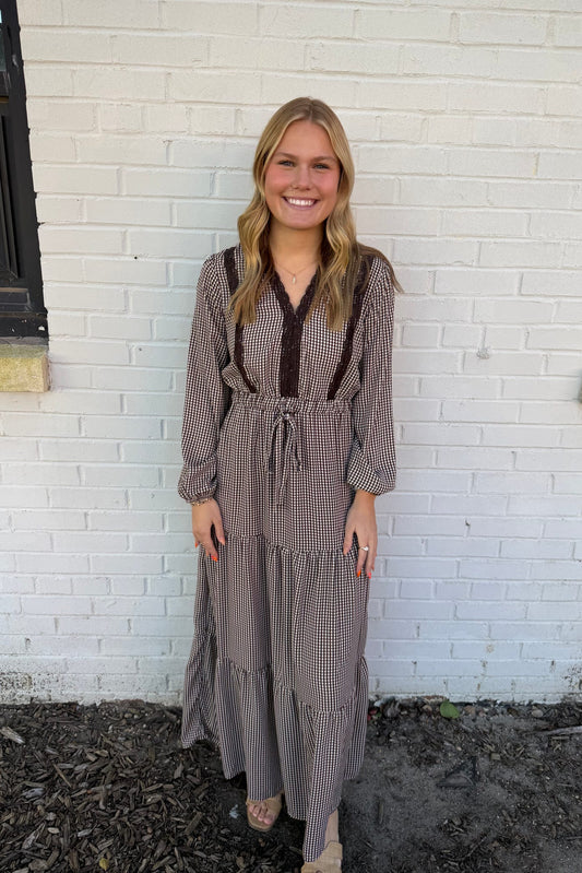Woman wearing a long, patterned dress standing against a white brick wall.