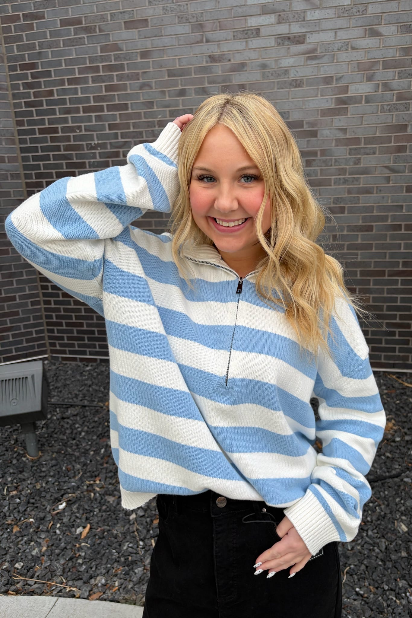 Woman wearing a blue and white striped sweater against a brick wall.