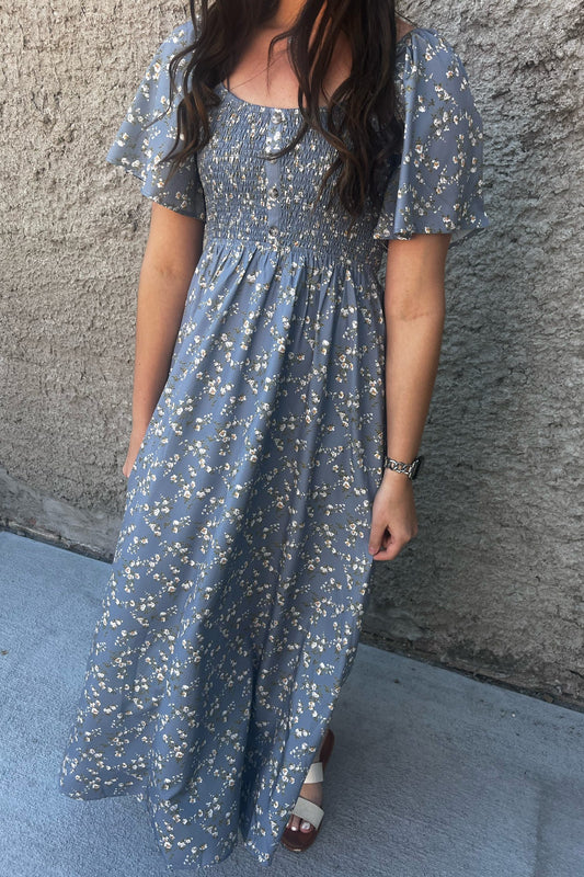 Person wearing a blue floral dress against a gray wall.