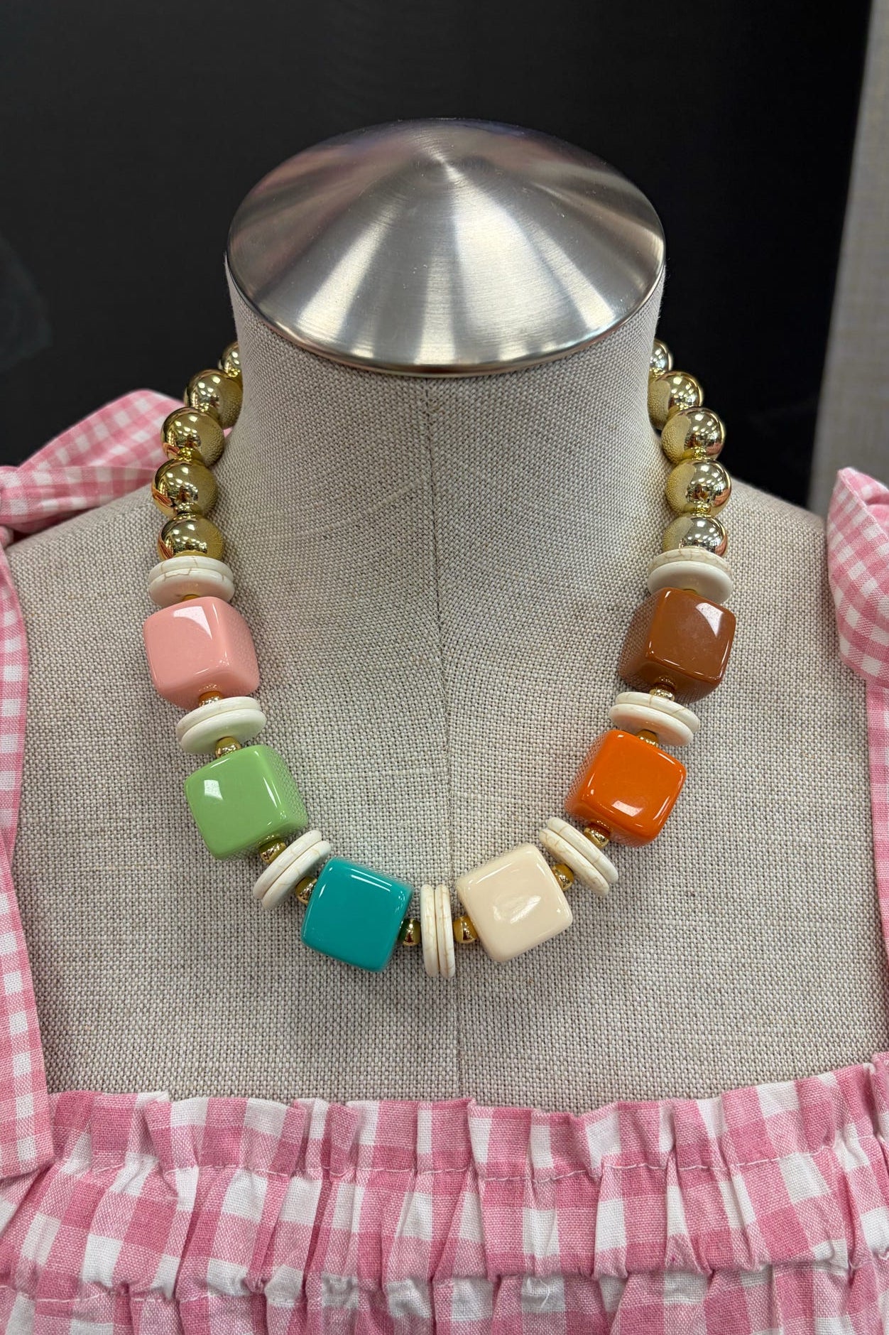 Colorful bead necklace on a mannequin bust with a pink checkered garment.