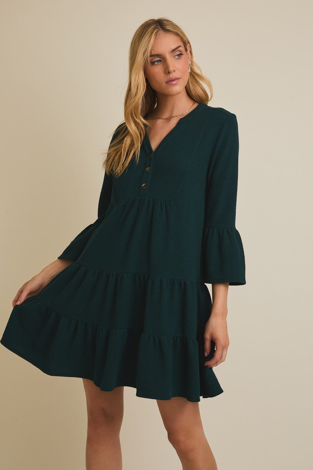 Woman wearing a dark green dress with long sleeves on a beige background