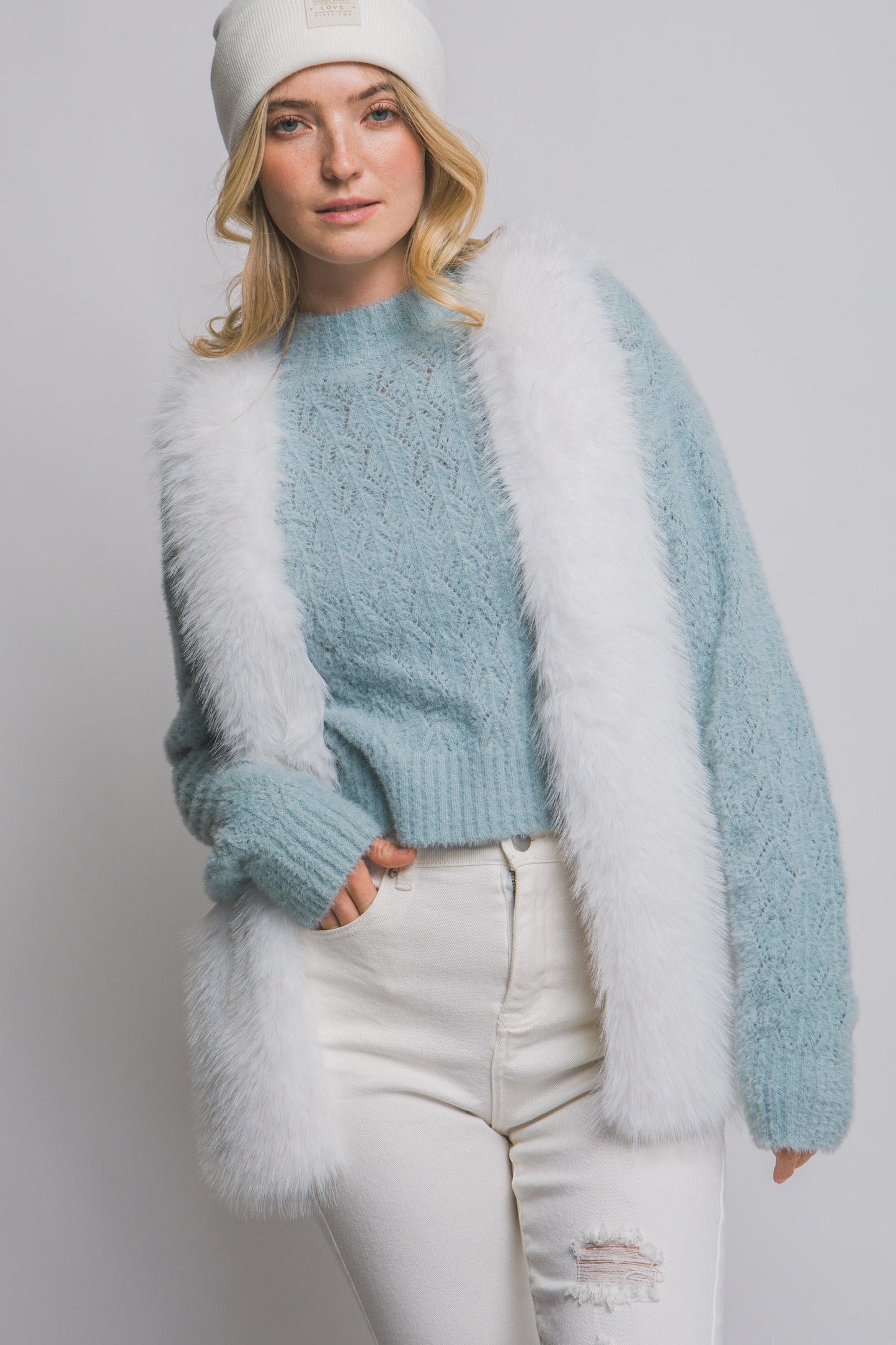 Woman wearing a light blue sweater with white fur trim against a plain background