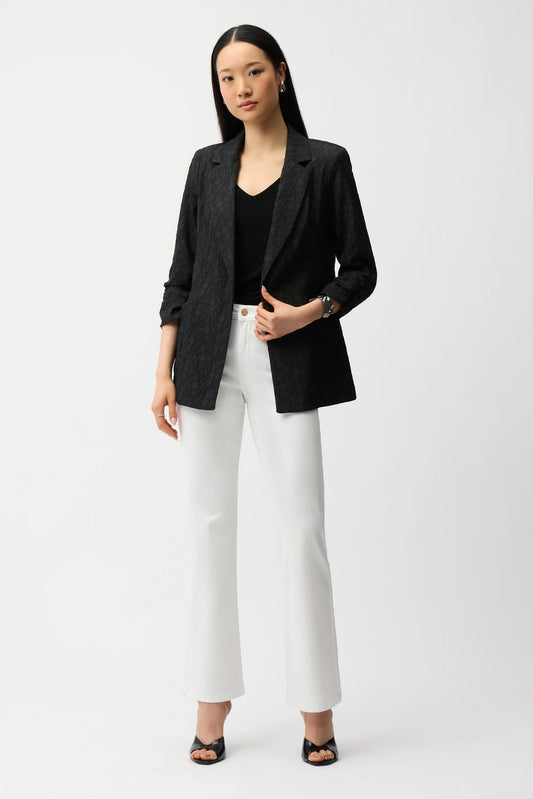 Woman wearing a black blazer, black top, and white pants on a white background