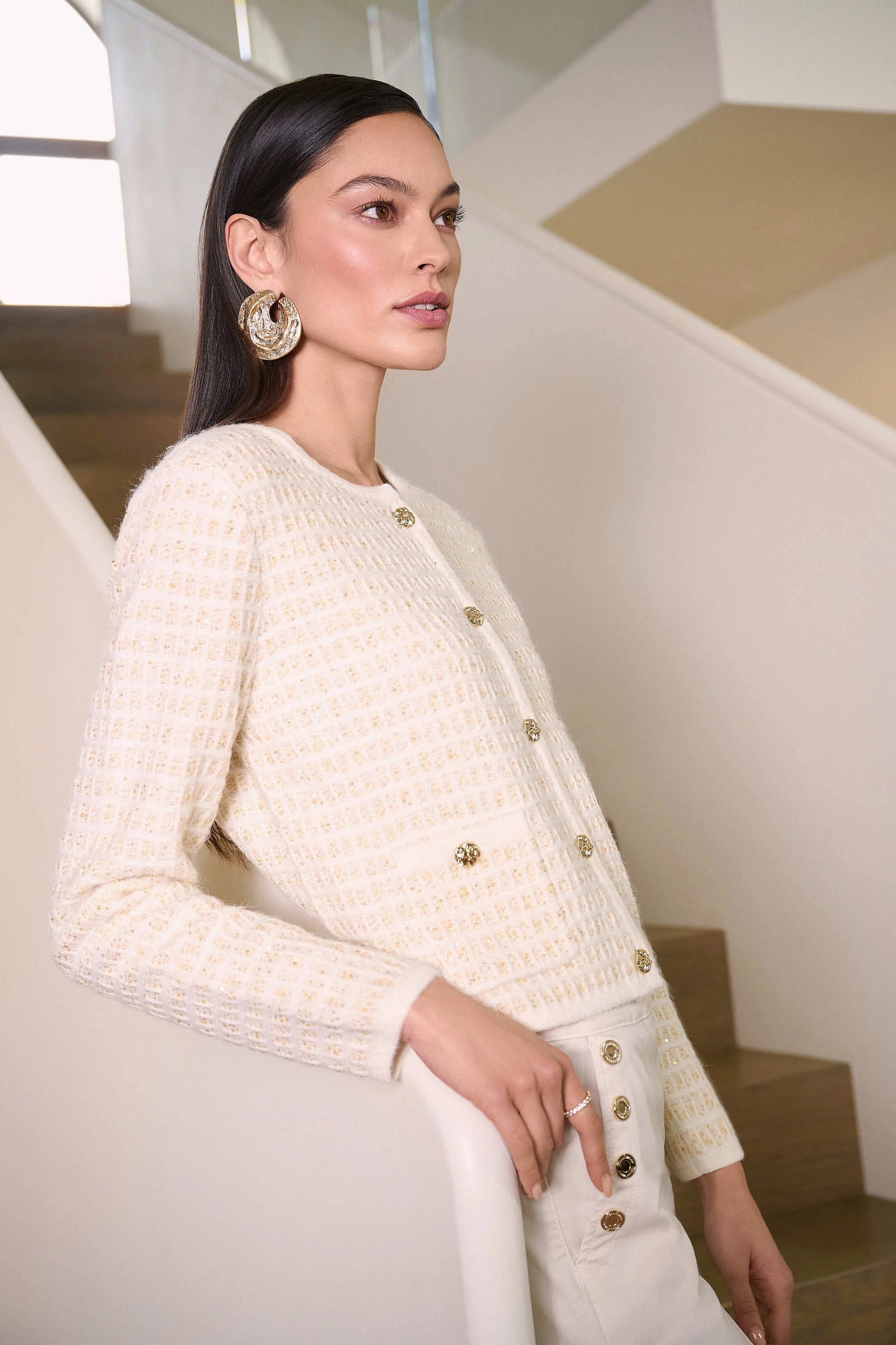 Woman wearing a cream-colored textured jacket with gold buttons in an indoor setting.