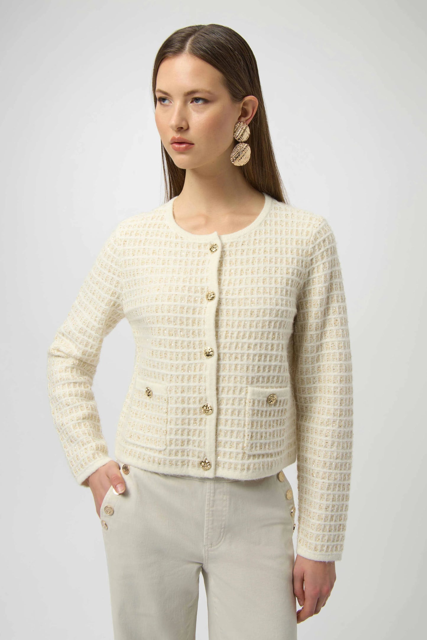 Woman wearing a textured cream jacket with gold buttons on a plain background