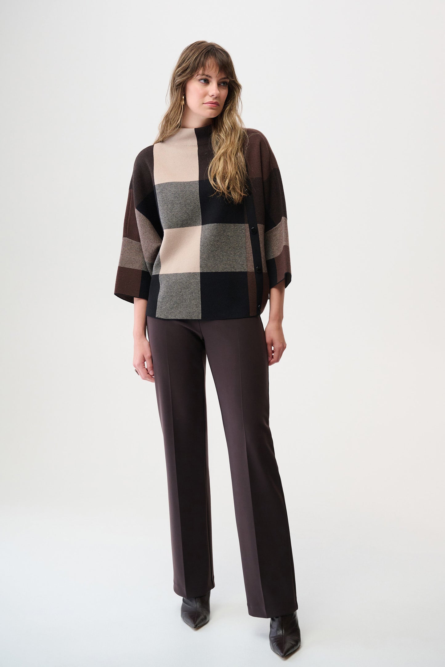 Woman wearing a checkered sweater over a black top with brown pants on a white background
