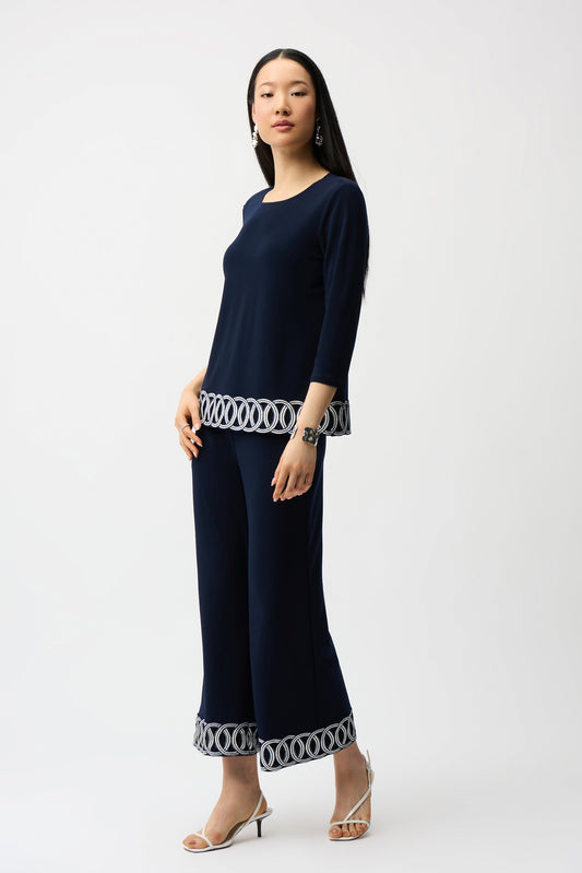 Woman wearing a navy outfit with patterned cuffs on a white background