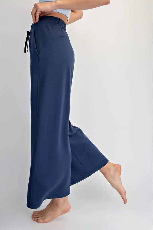 A person wearing wide-leg navy blue lounge pants with a drawstring waist, shown from the waist down against a plain light gray studio background.