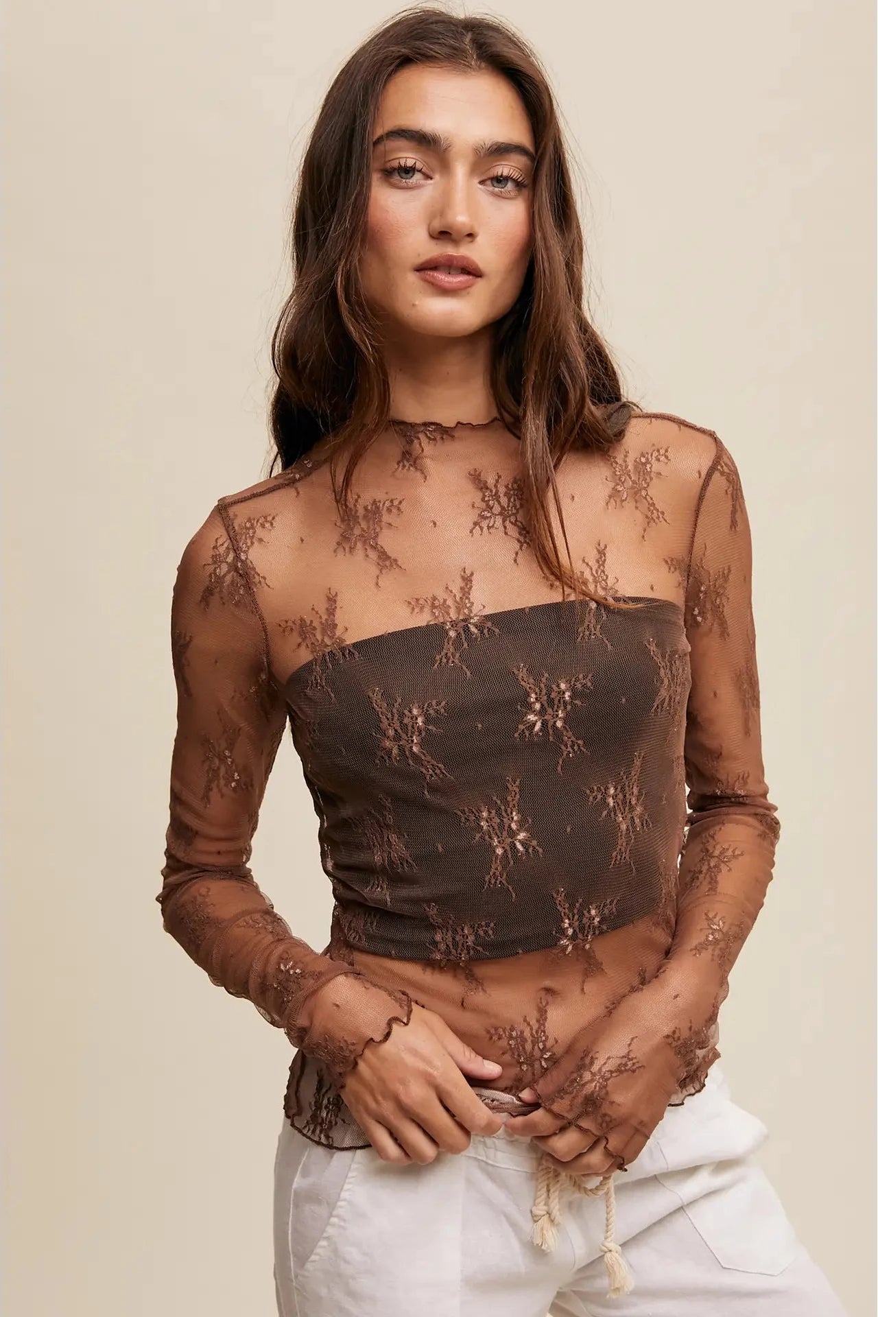 Woman wearing a sheer brown top with floral patterns on a beige background