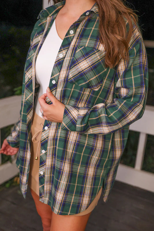 Person wearing a green plaid shirt over a white top outdoors.
