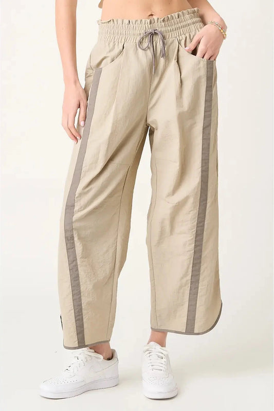Beige pants with gray side stripes worn by a person on a white background