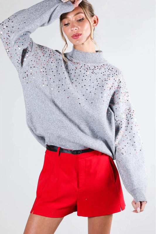 Person wearing a gray sweater with black speckles and red shorts on a white background
