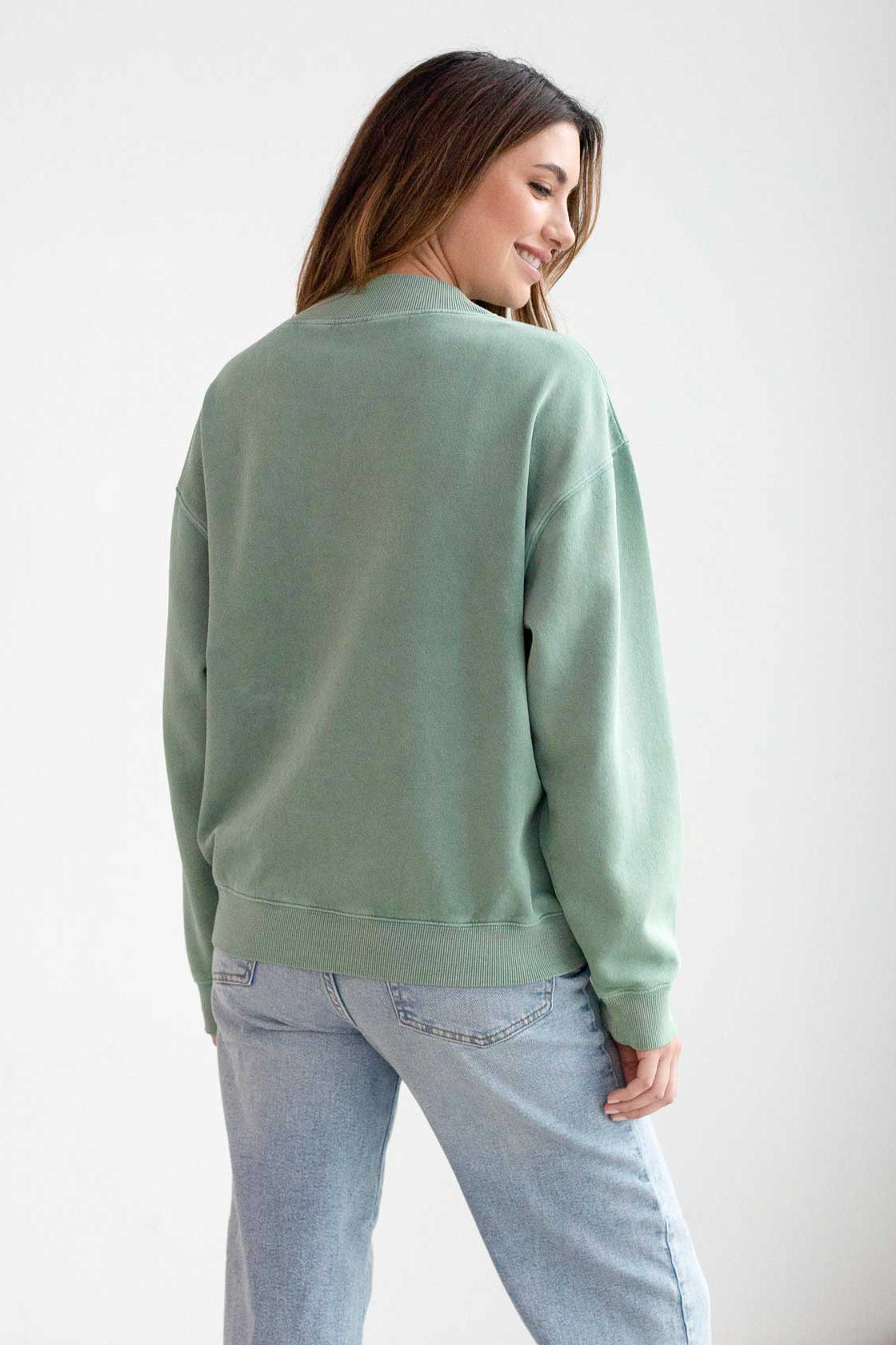 Woman wearing a green sweatshirt and light blue jeans on a white background