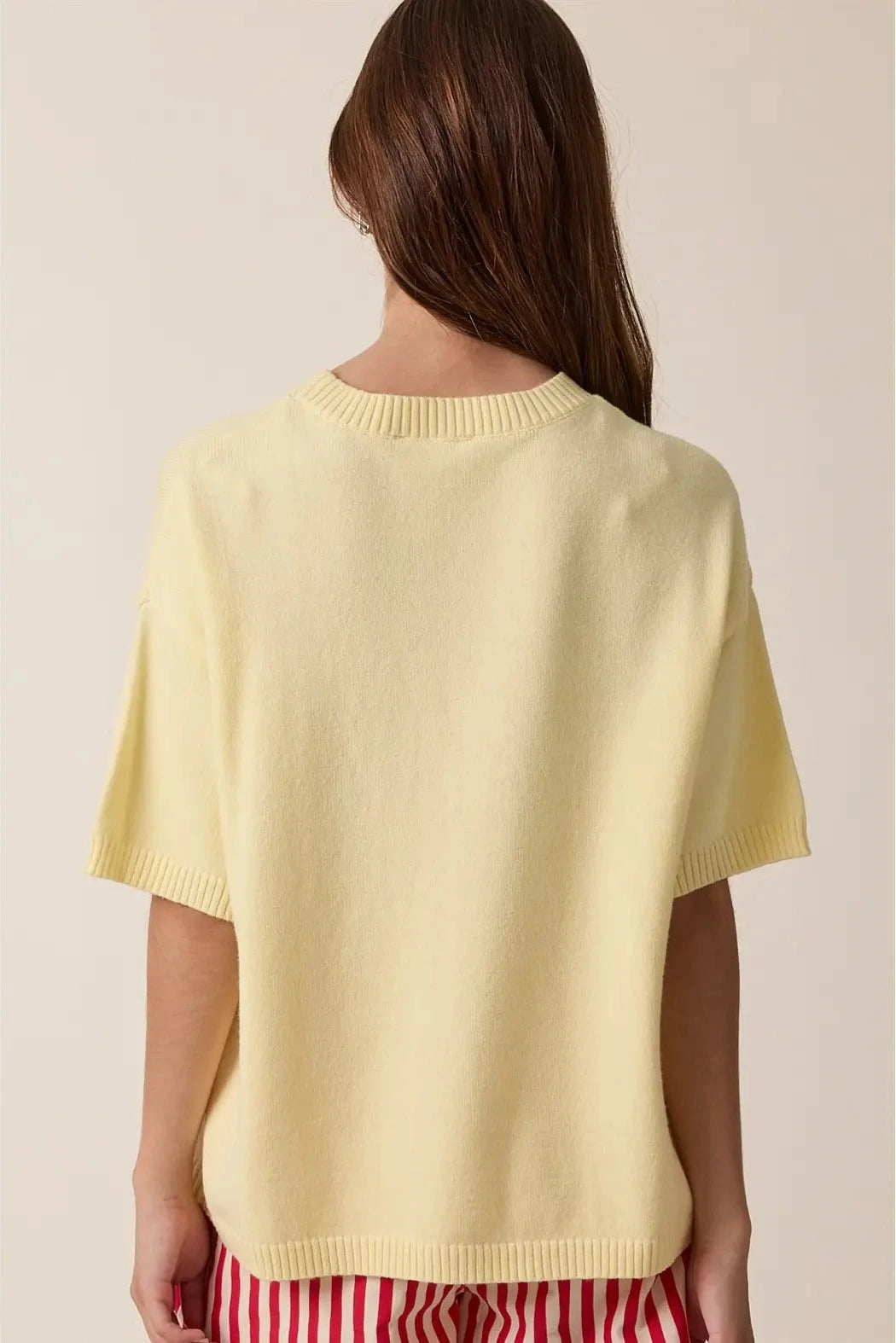 Person wearing a light yellow sweater over a red and white striped garment on a beige background