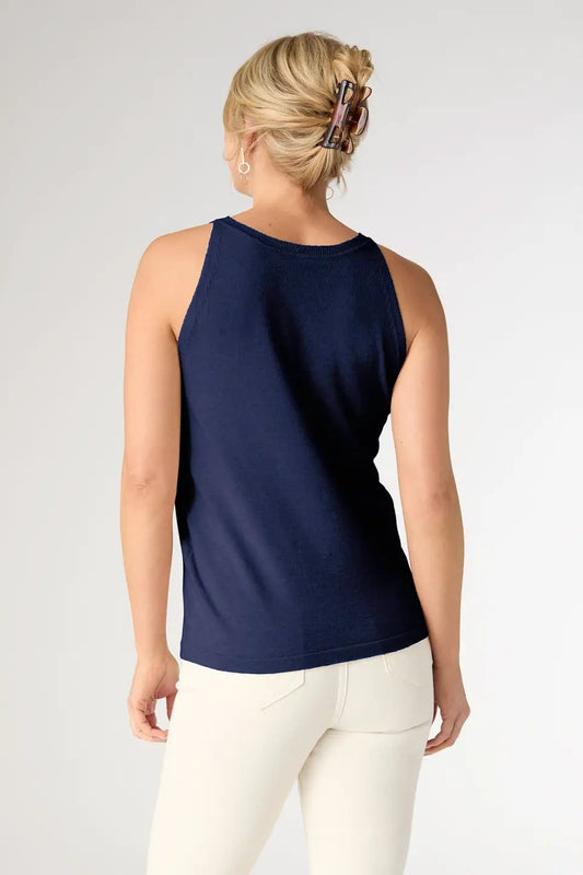 Woman wearing a navy blue sleeveless top and white pants on a light gray background