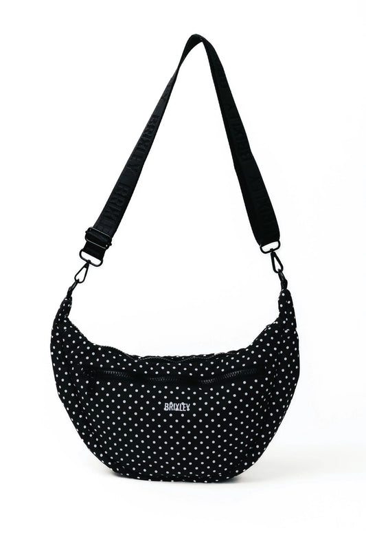 A black crescent-shaped shoulder bag with white polka dots and a black adjustable strap, featuring a small silver 'society' logo on the front, set against a plain white background.