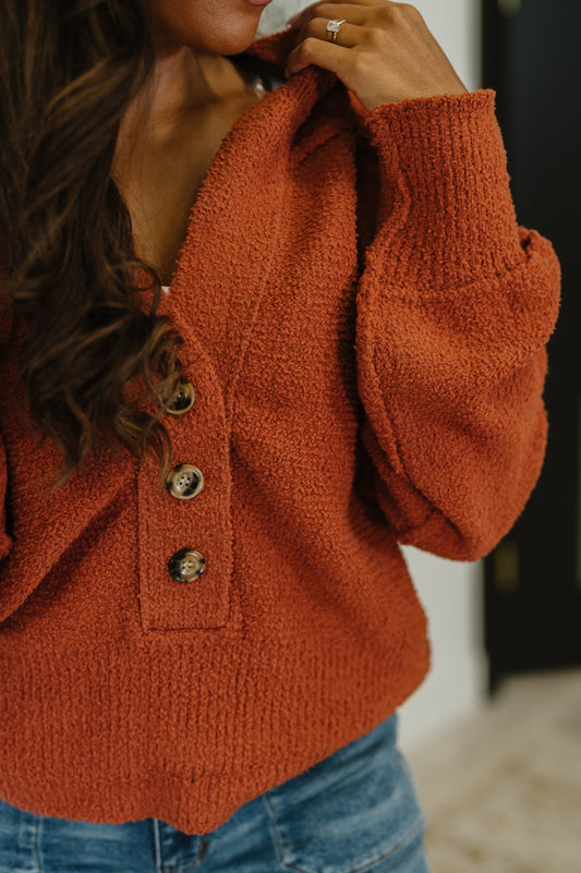 Close-up of a person wearing a rust-colored knitted cardigan with gold buttons.