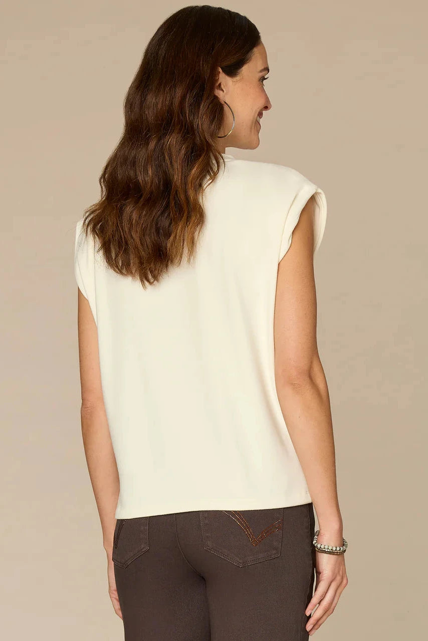 Woman wearing a white sleeveless top and brown pants on a beige background