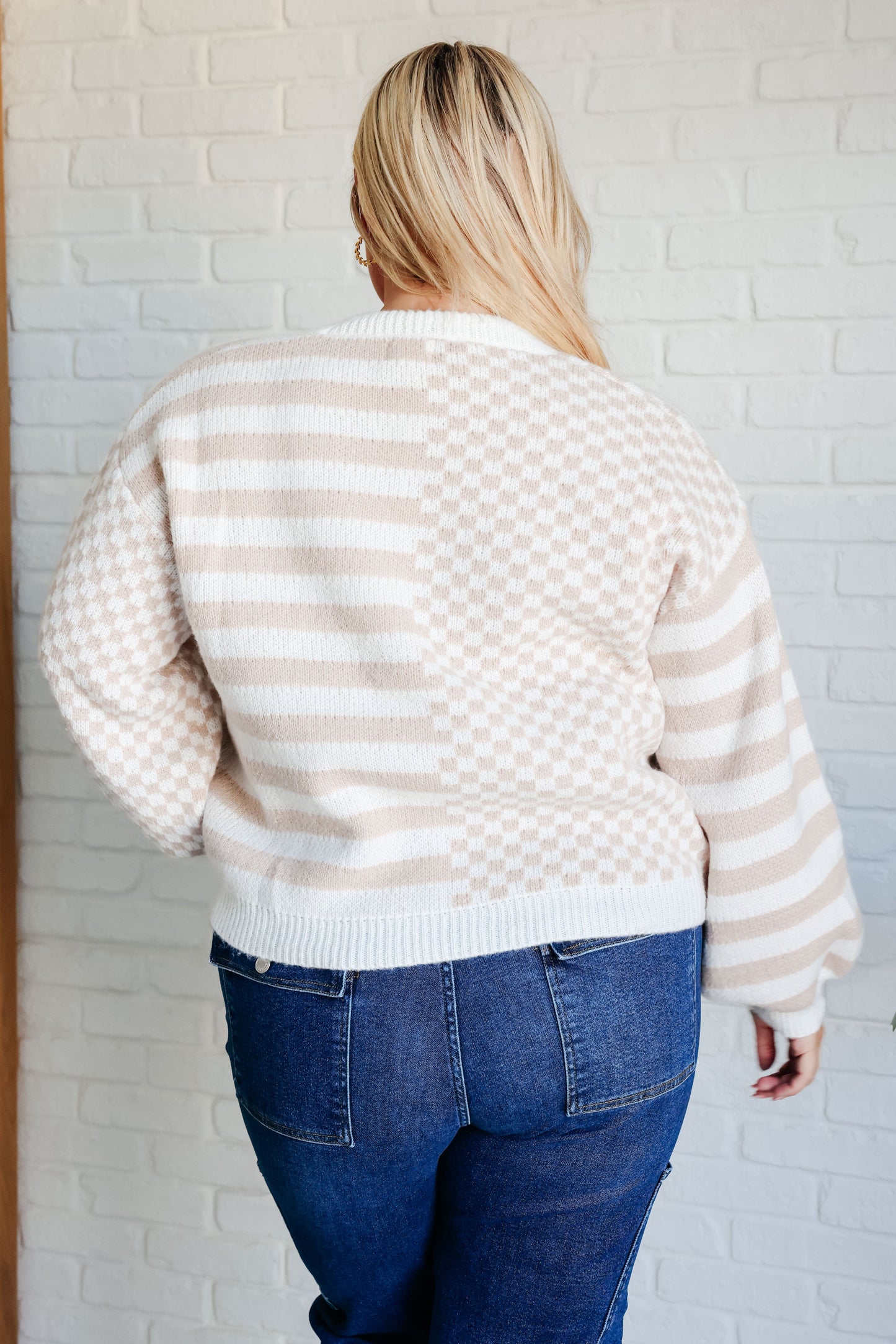 Person wearing a beige and white striped sweater and blue jeans against a white brick wall.