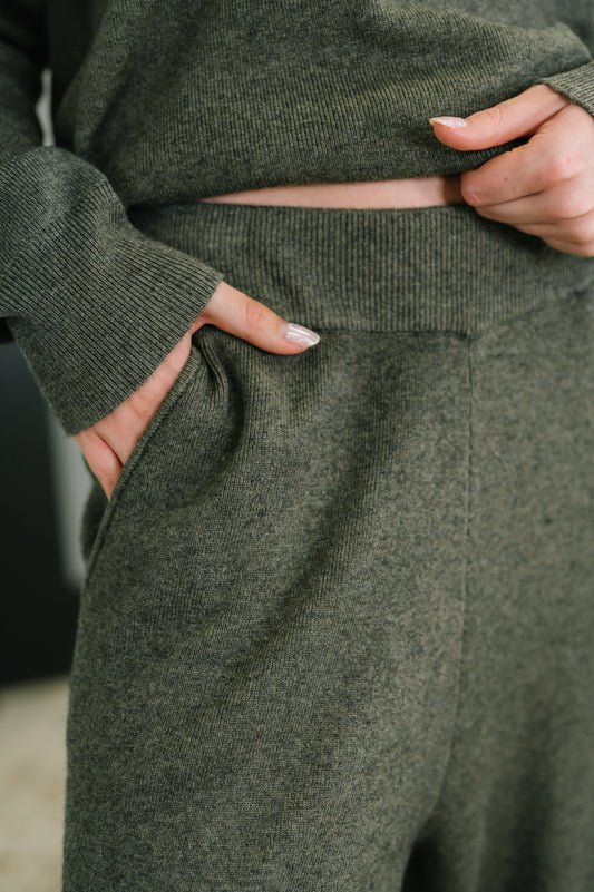 Person wearing green fleece pants with hands in the pockets, blurred background