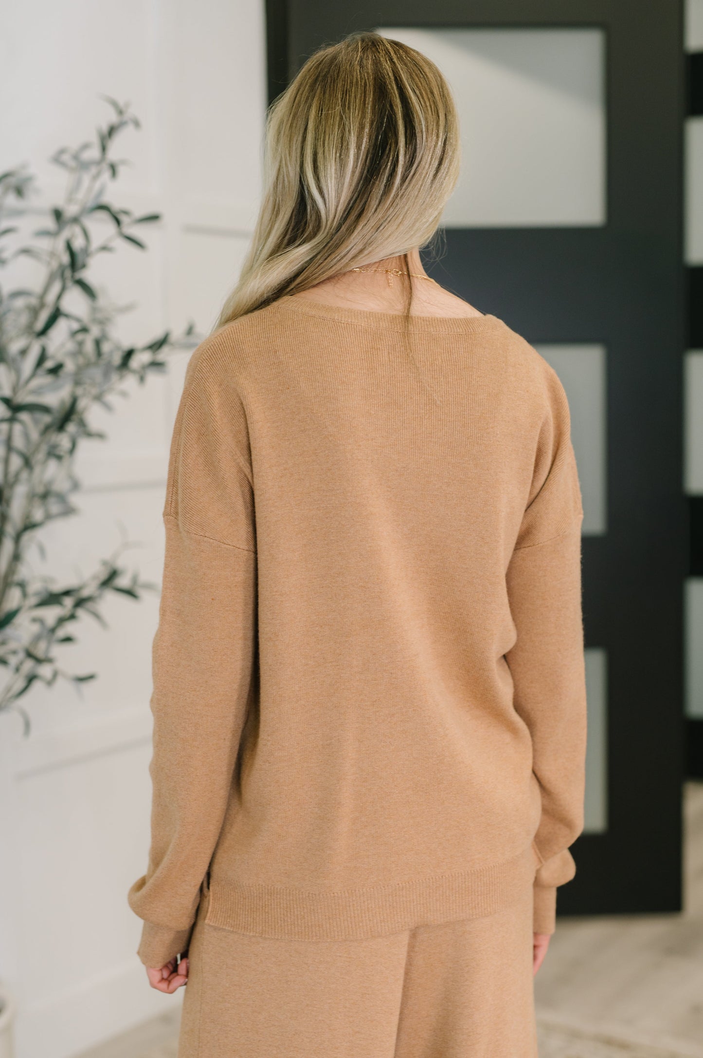 Person wearing a tan sweater and pants in a minimal indoor setting