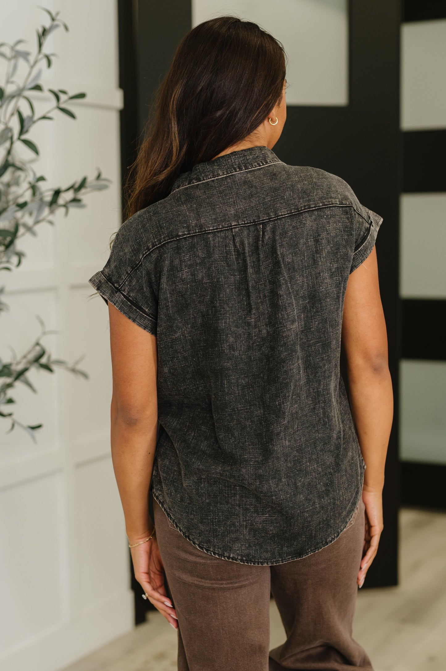 Woman wearing a sleeveless black denim shirt in an indoor setting.