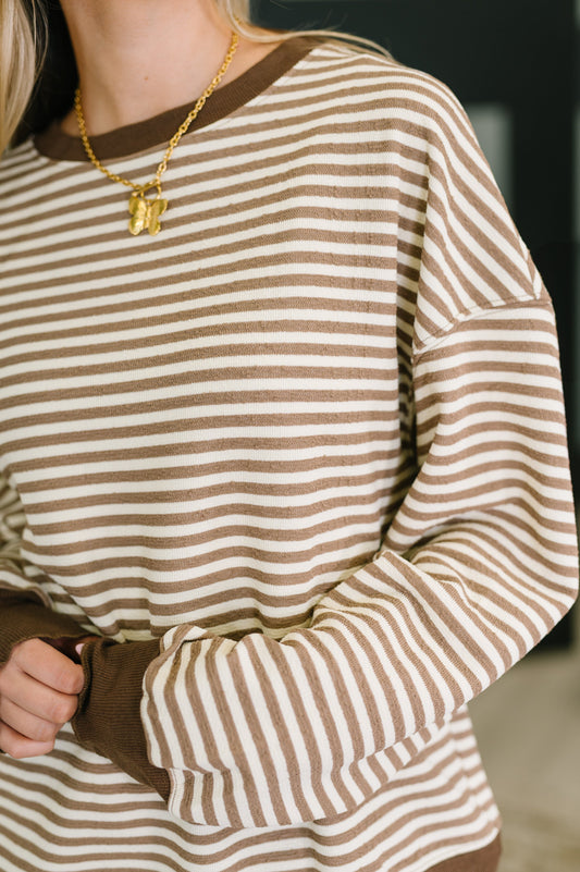 Close-up of a person wearing a brown and white striped sweater with a gold necklace.