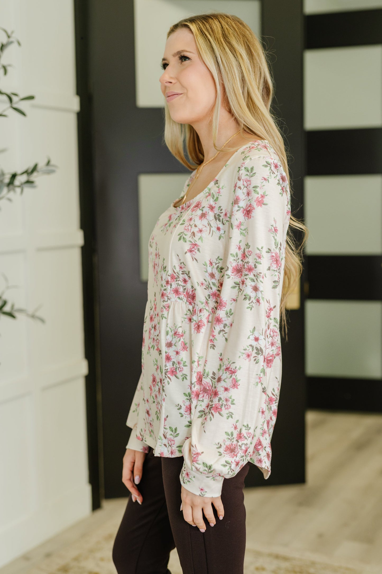 Woman wearing a floral blouse standing indoors with a neutral background