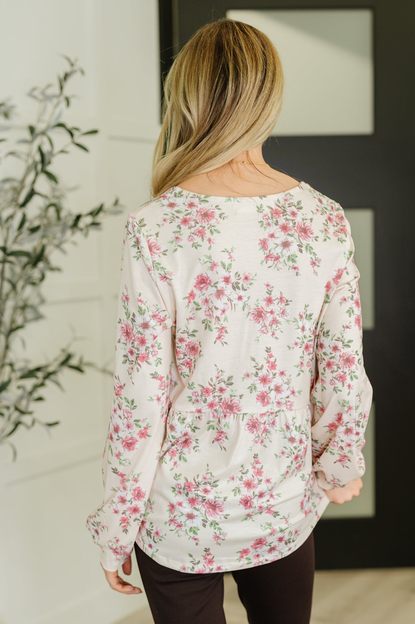 Person wearing a floral blouse in a room with a plant and framed picture.