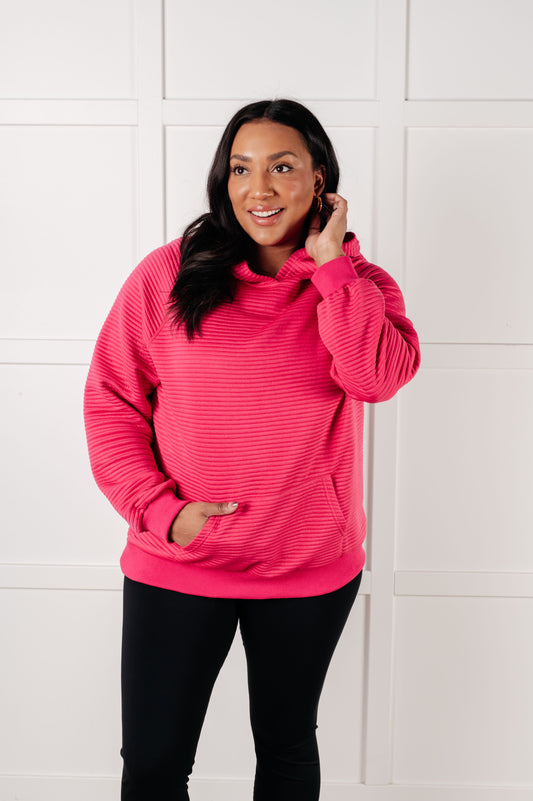 Woman wearing a bright pink hoodie against a white tiled wall