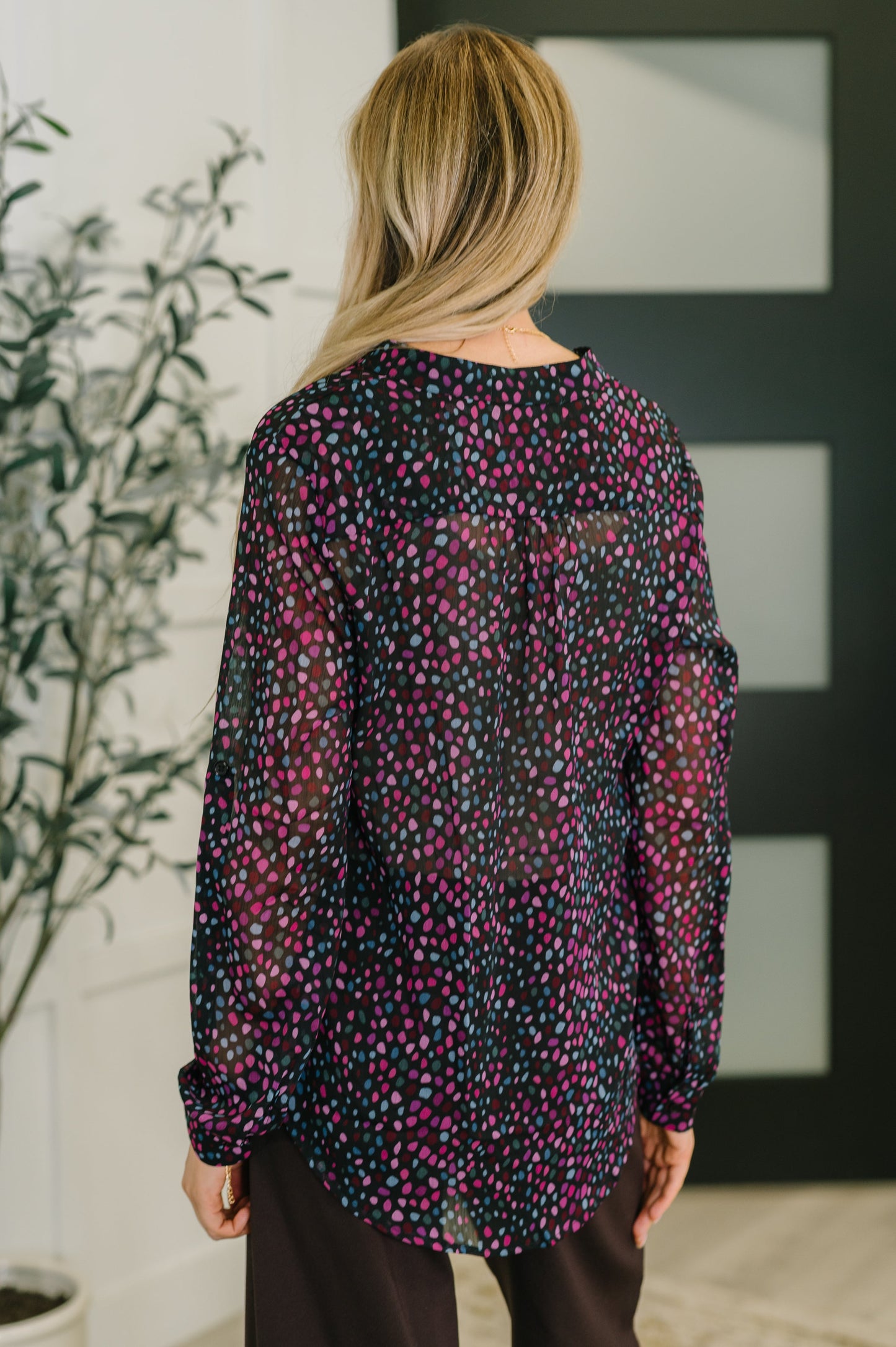 Person wearing a long-sleeve, patterned blouse in a room with a plant and abstract wall art.