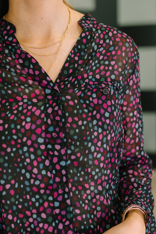 Close-up of a person wearing a patterned blouse with pink and blue dots on a black background.