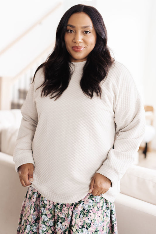 Woman wearing a light gray sweater and floral pants indoors