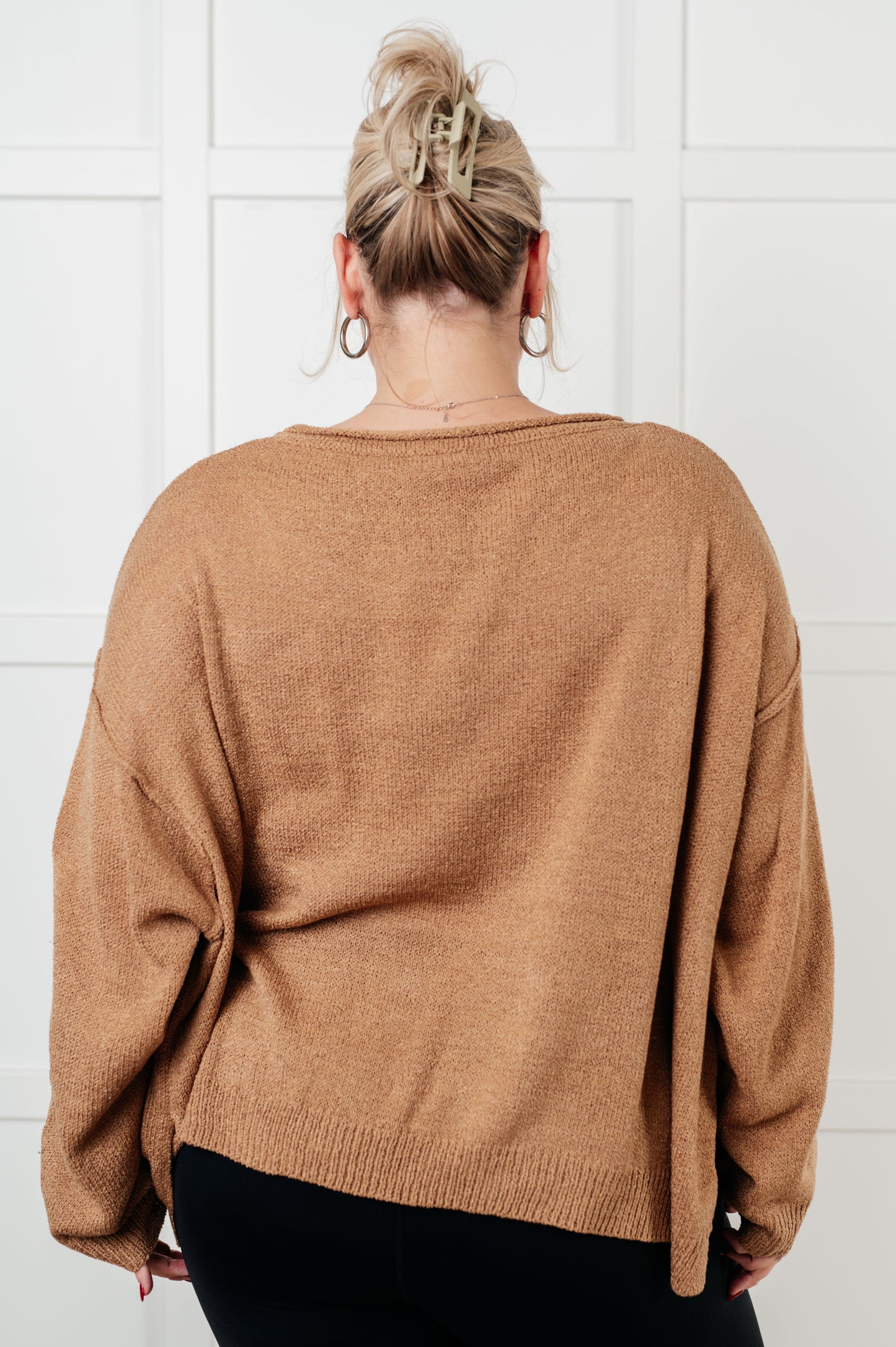 Person wearing a brown sweater against a white tiled wall
