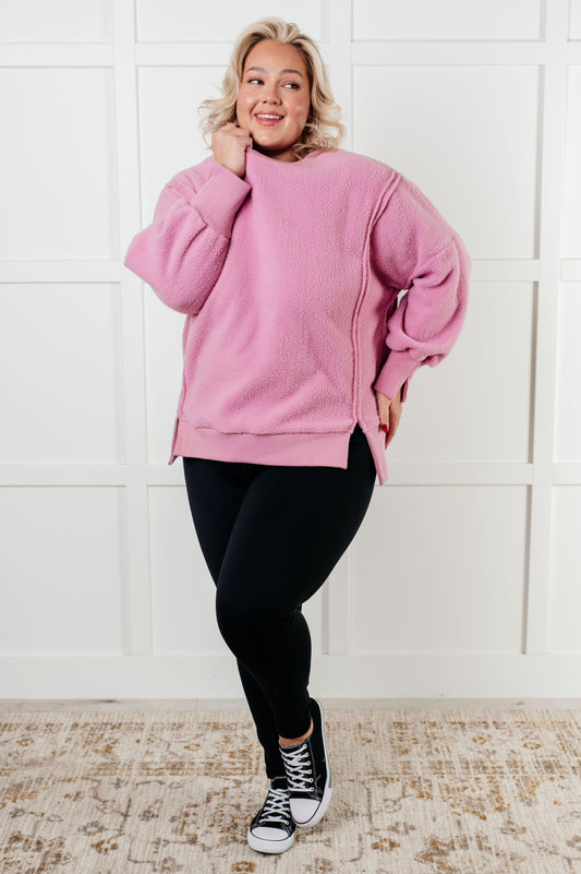 Person wearing a pink sweater and black leggings standing against a white wall.