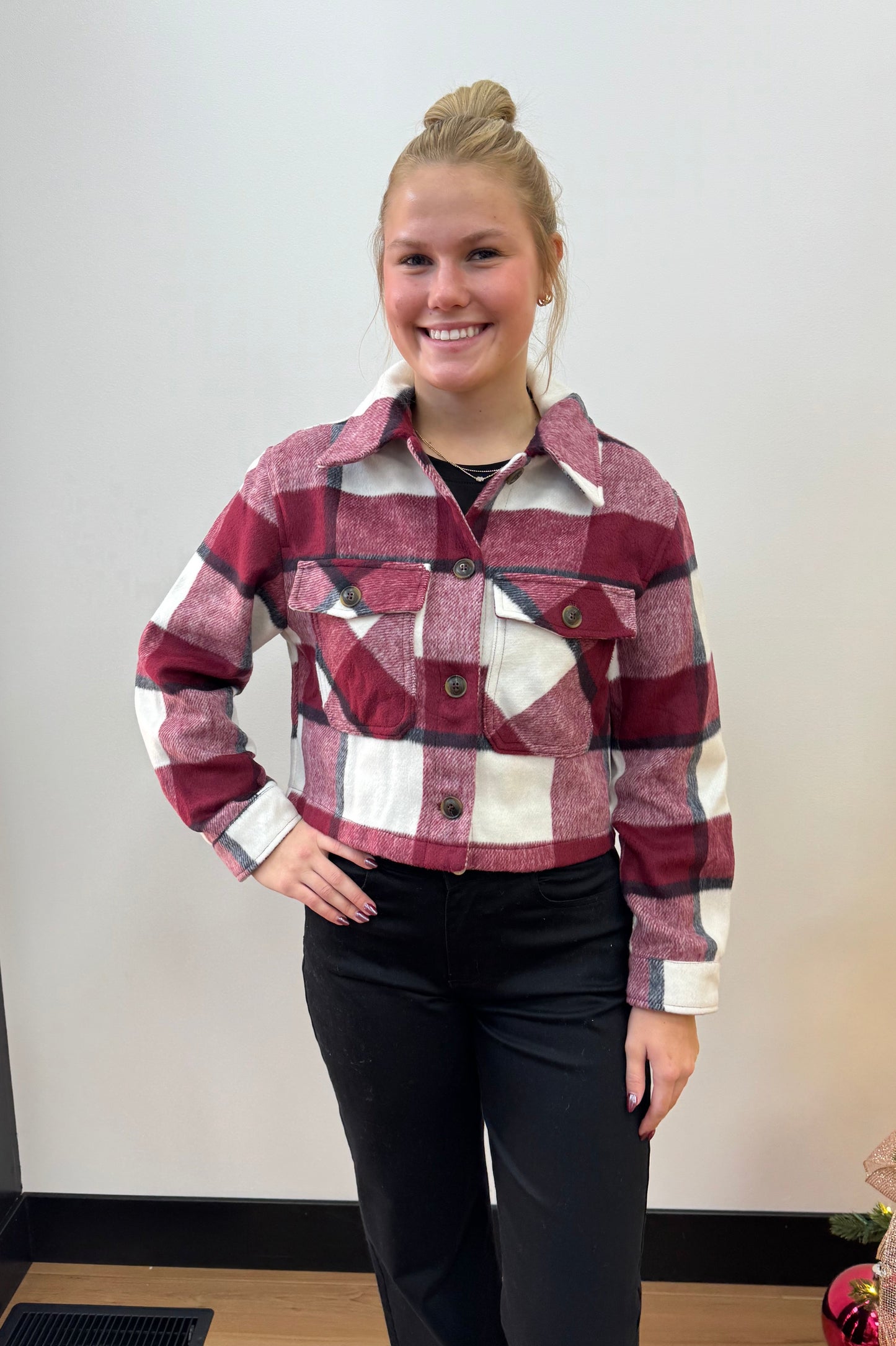 Person wearing a plaid shirt standing in front of a white wall with a Christmas tree in the background.