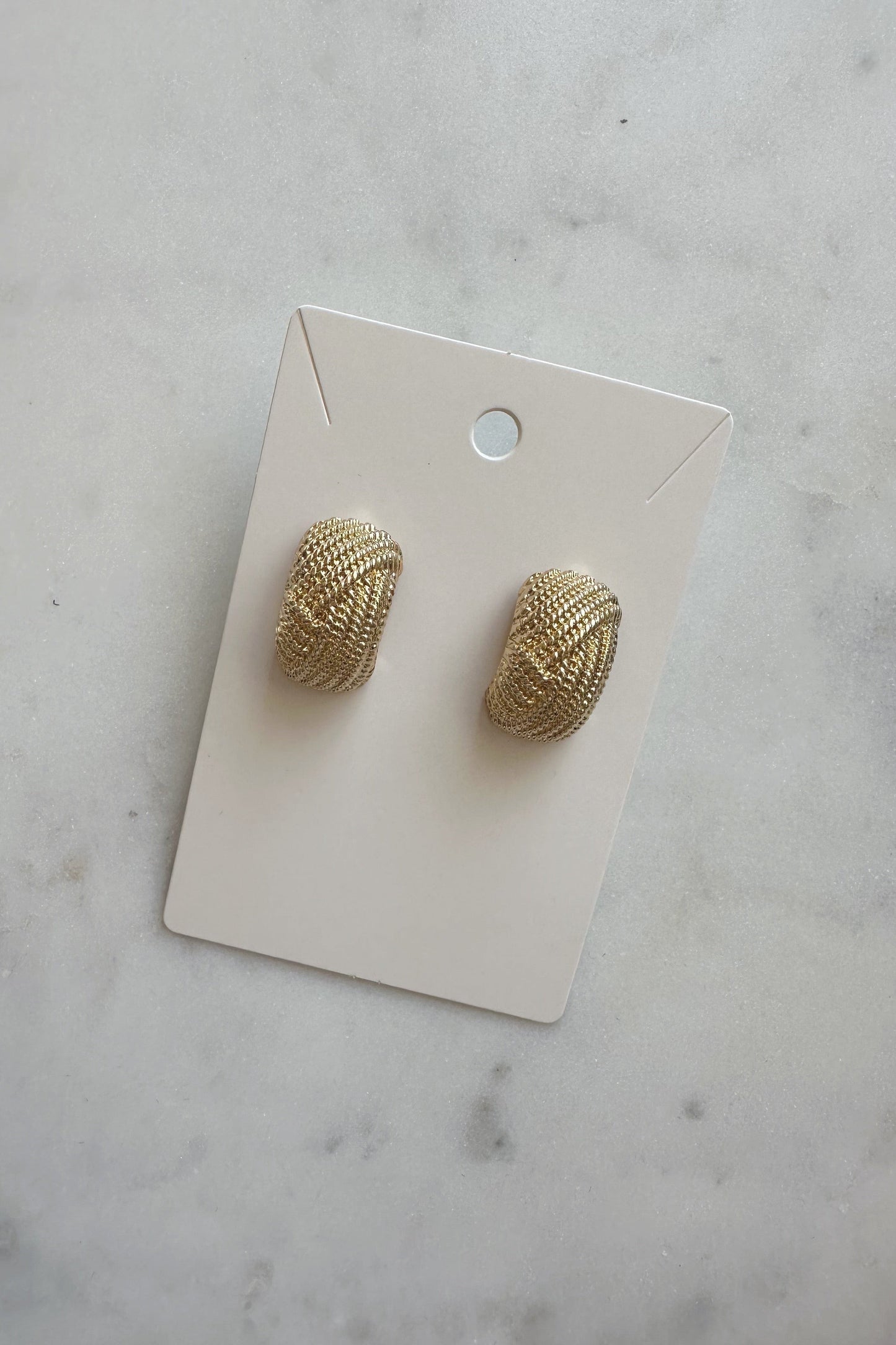A pair of gold textured metallic wide shield earrings on a white card.