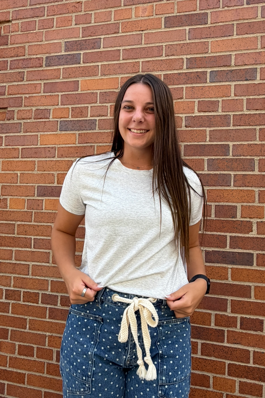 A woman stands in front of a red brick wall wearing a light gray short-sleeve t-shirt and blue polka-dot drawstring pants.