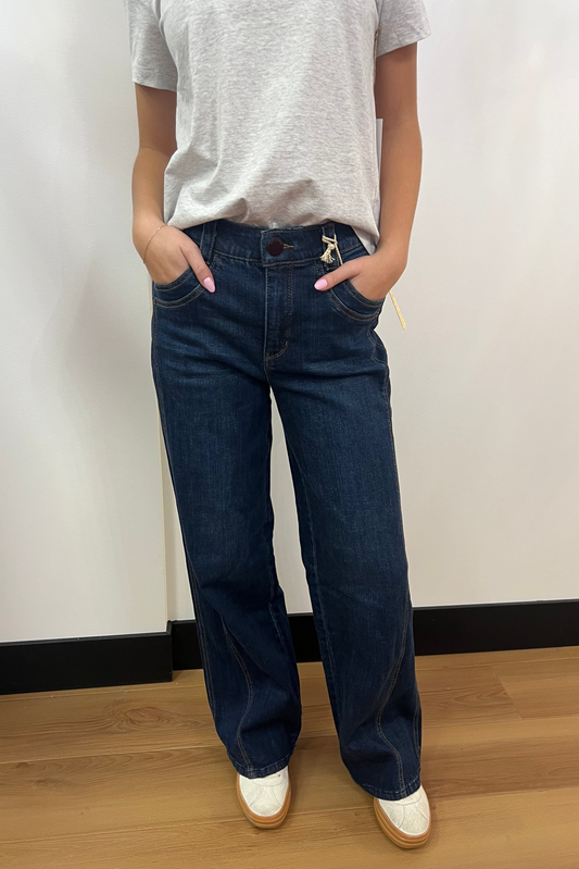 Person wearing dark blue jeans and a gray shirt against a white wall.