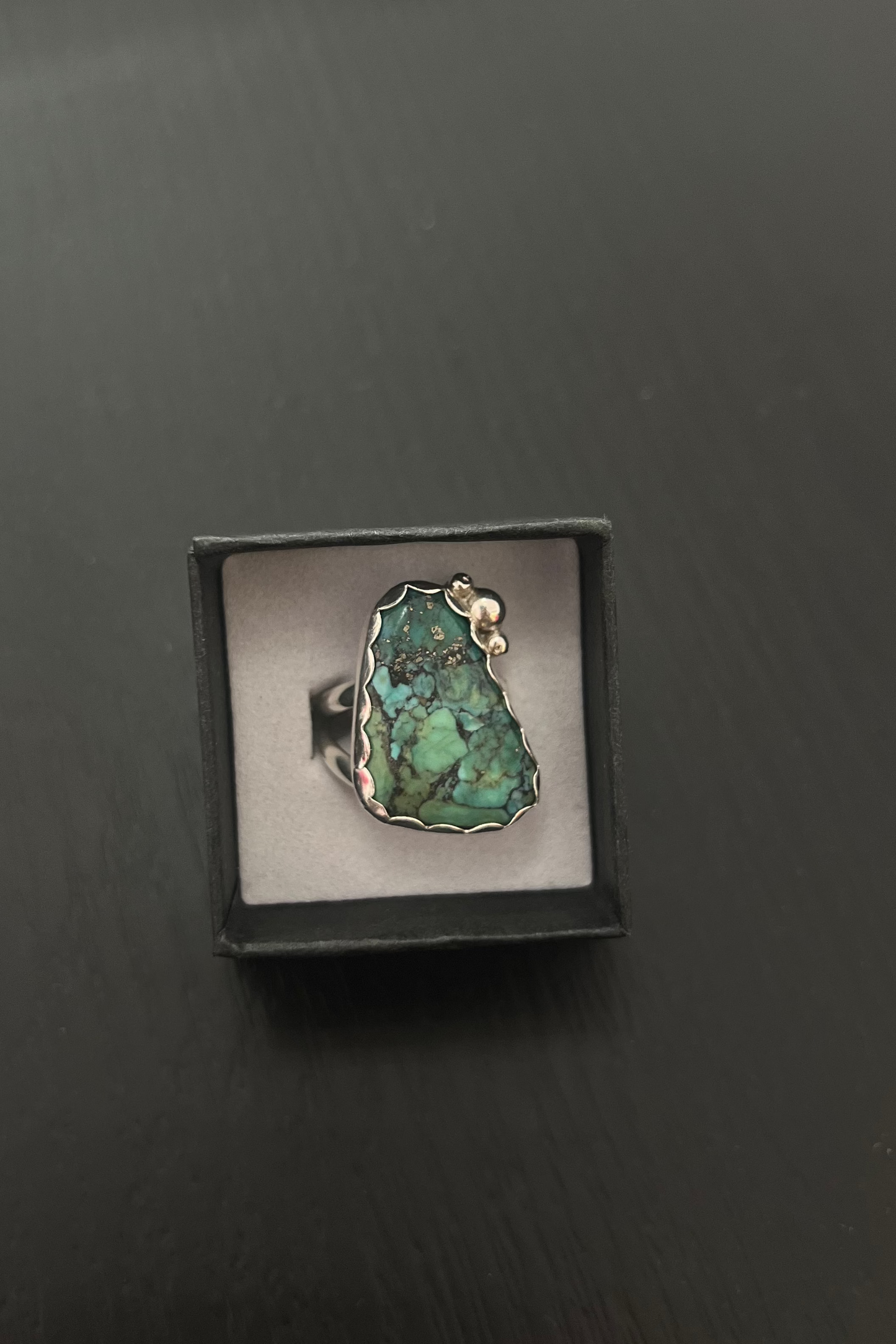 Ring with a green stone in a black box on a dark surface