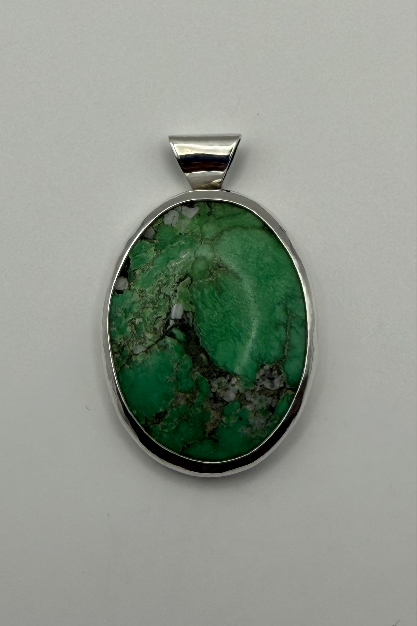 A green stone pendant, set in a polished sterling silver bezel with a bail, shown on a white background.