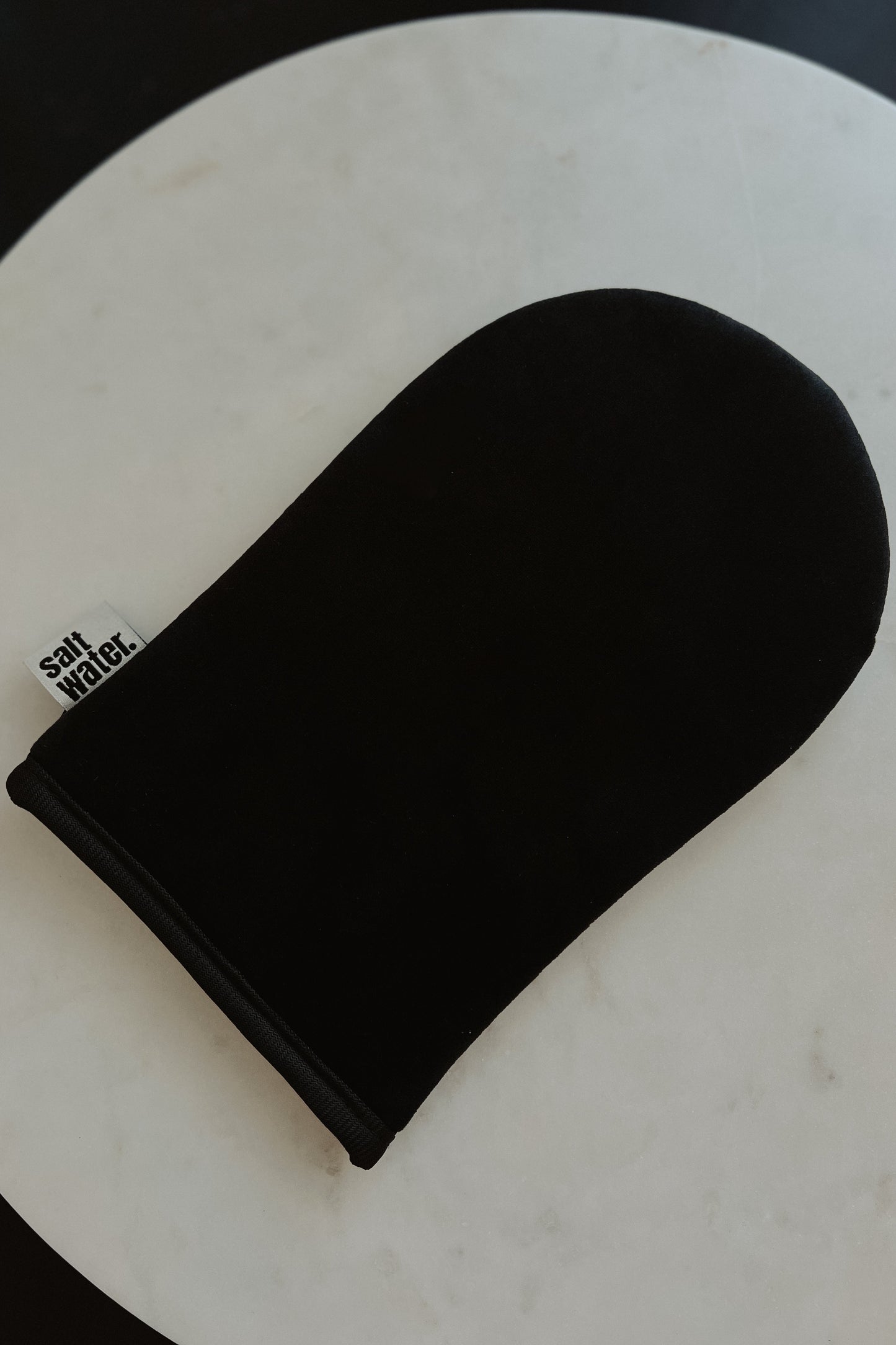 A black velvety application mitt for self-tan products