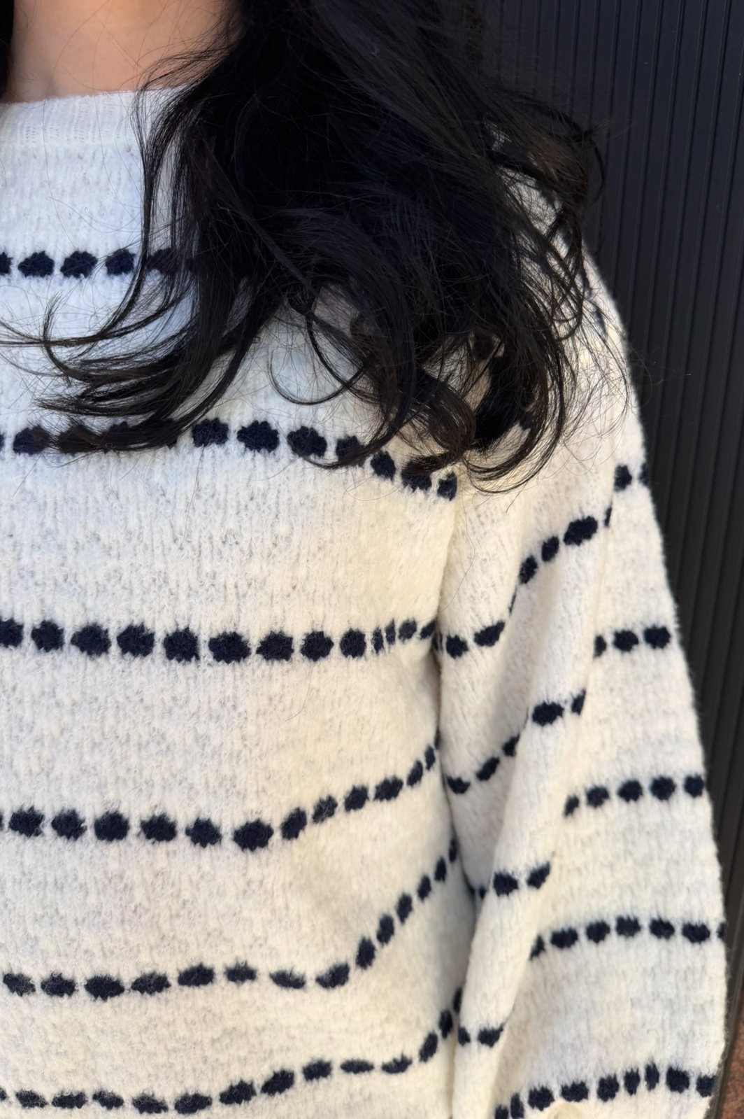 Person wearing a white sweater with navy polka dots, sitting on a dark surface.