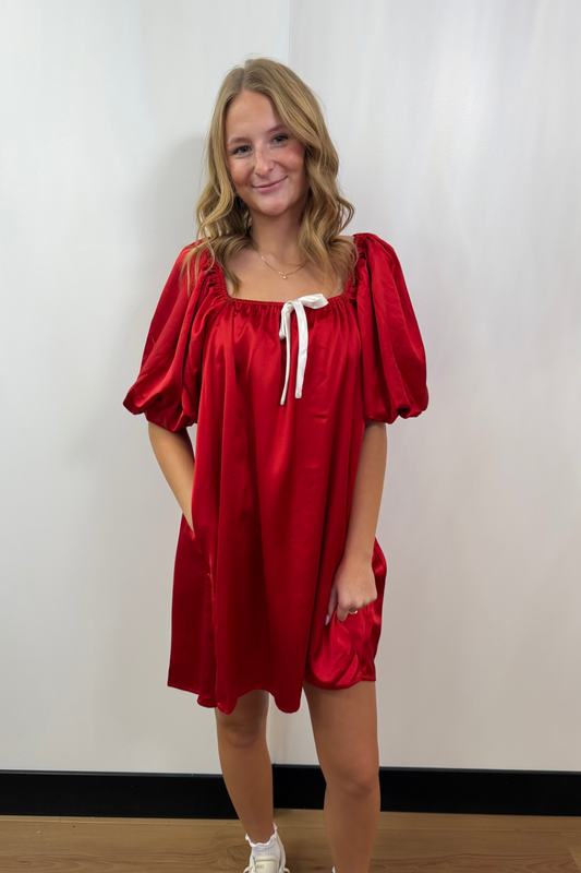 Woman wearing a red dress with puff sleeves against a white wall