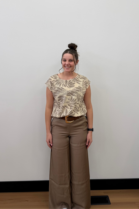 Woman standing against a plain white wall wearing a patterned top and wide-leg pants.