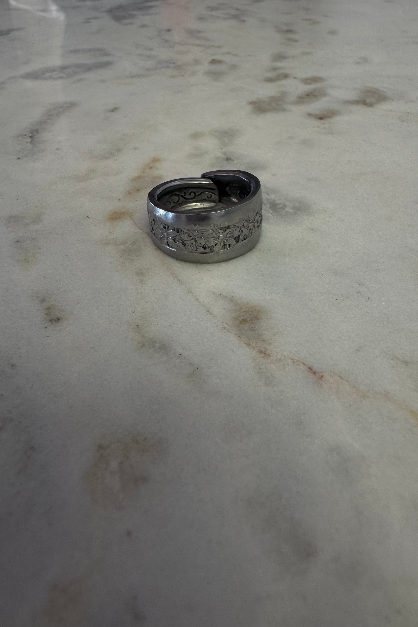 Silver ring with floral designs on a marbled surface